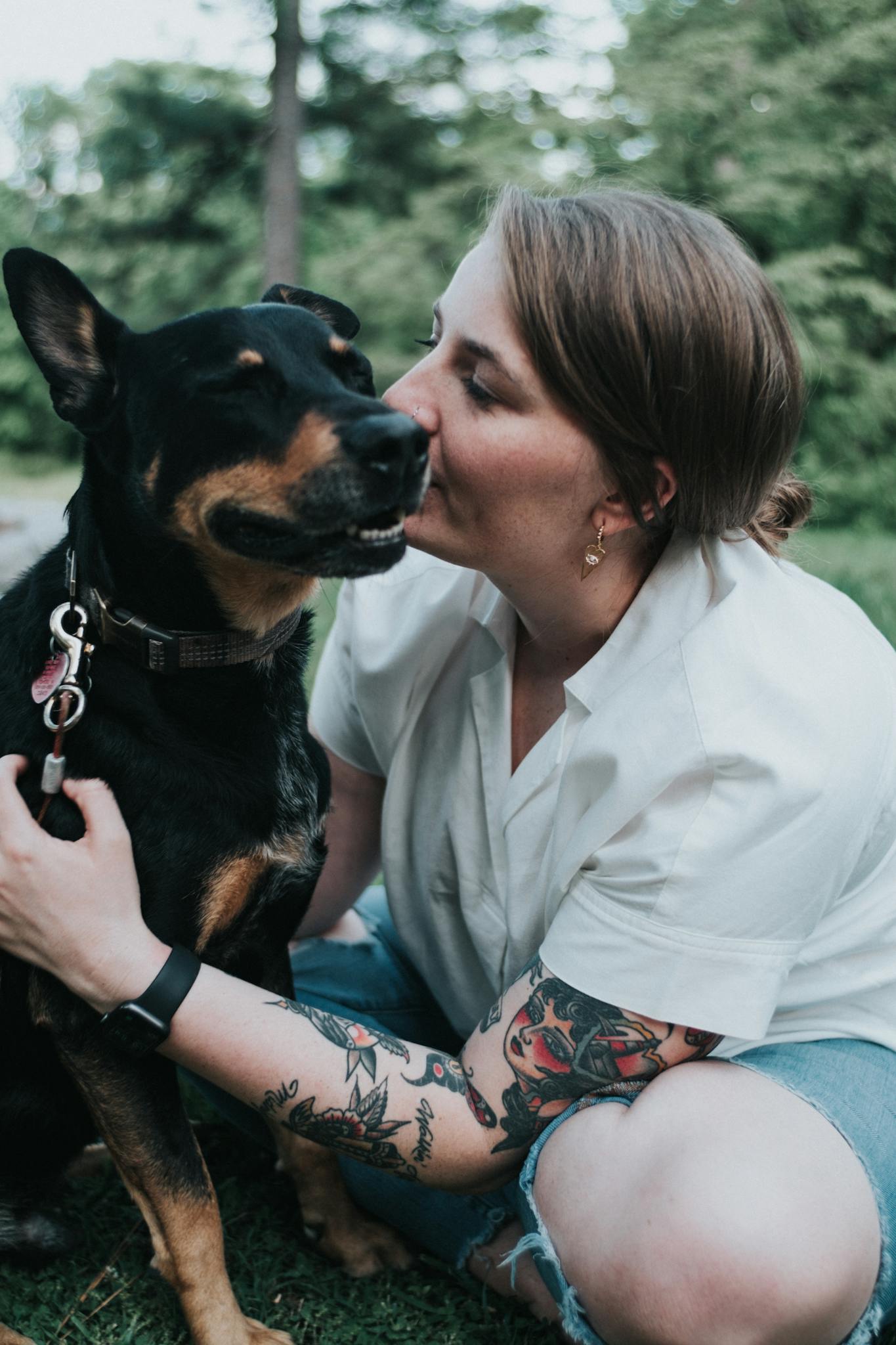 A woman lovingly kisses her Dobermann in a lush green park.
