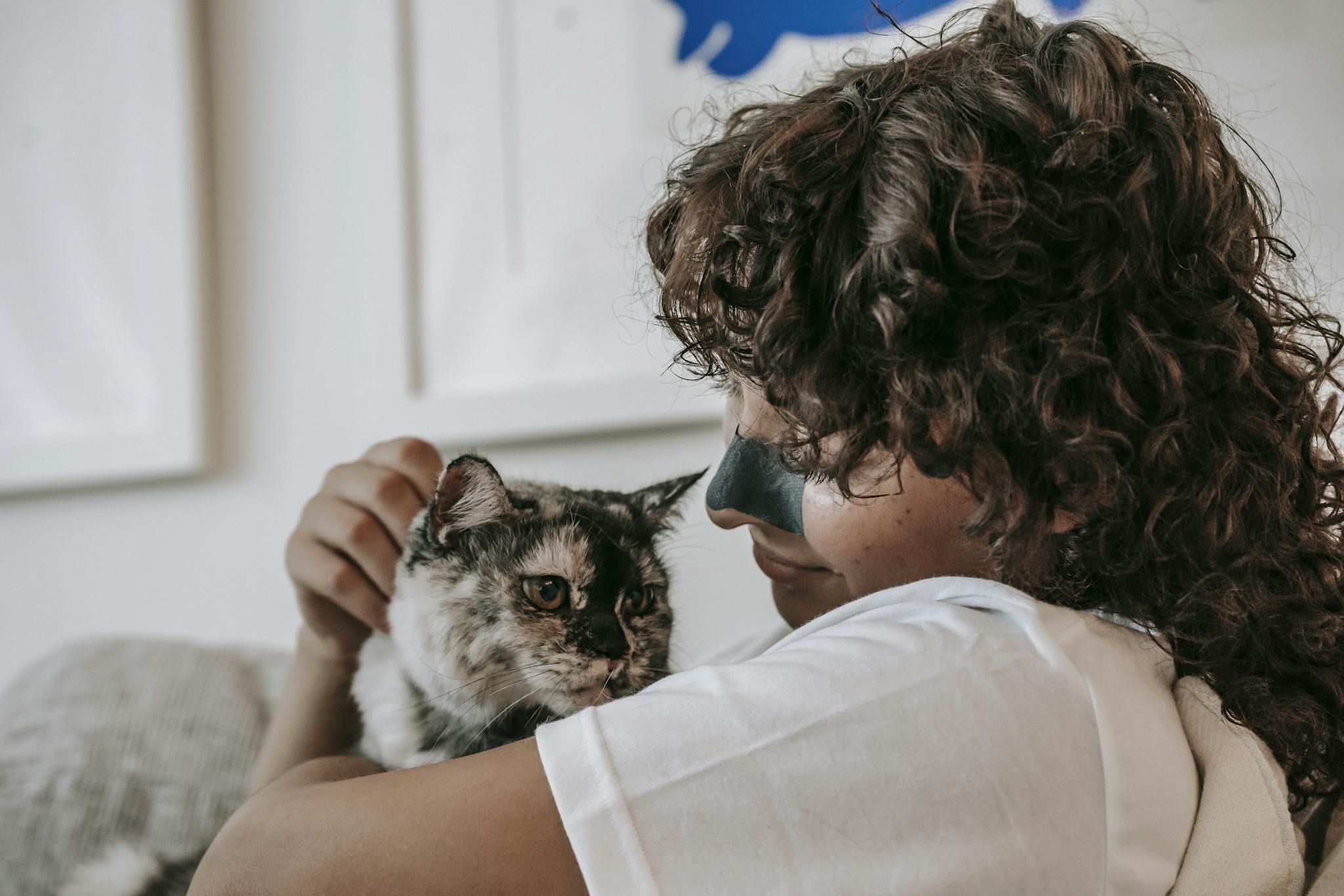 A woman smiling indoors while cuddling her furry pet cat. A moment of affection and companionship.