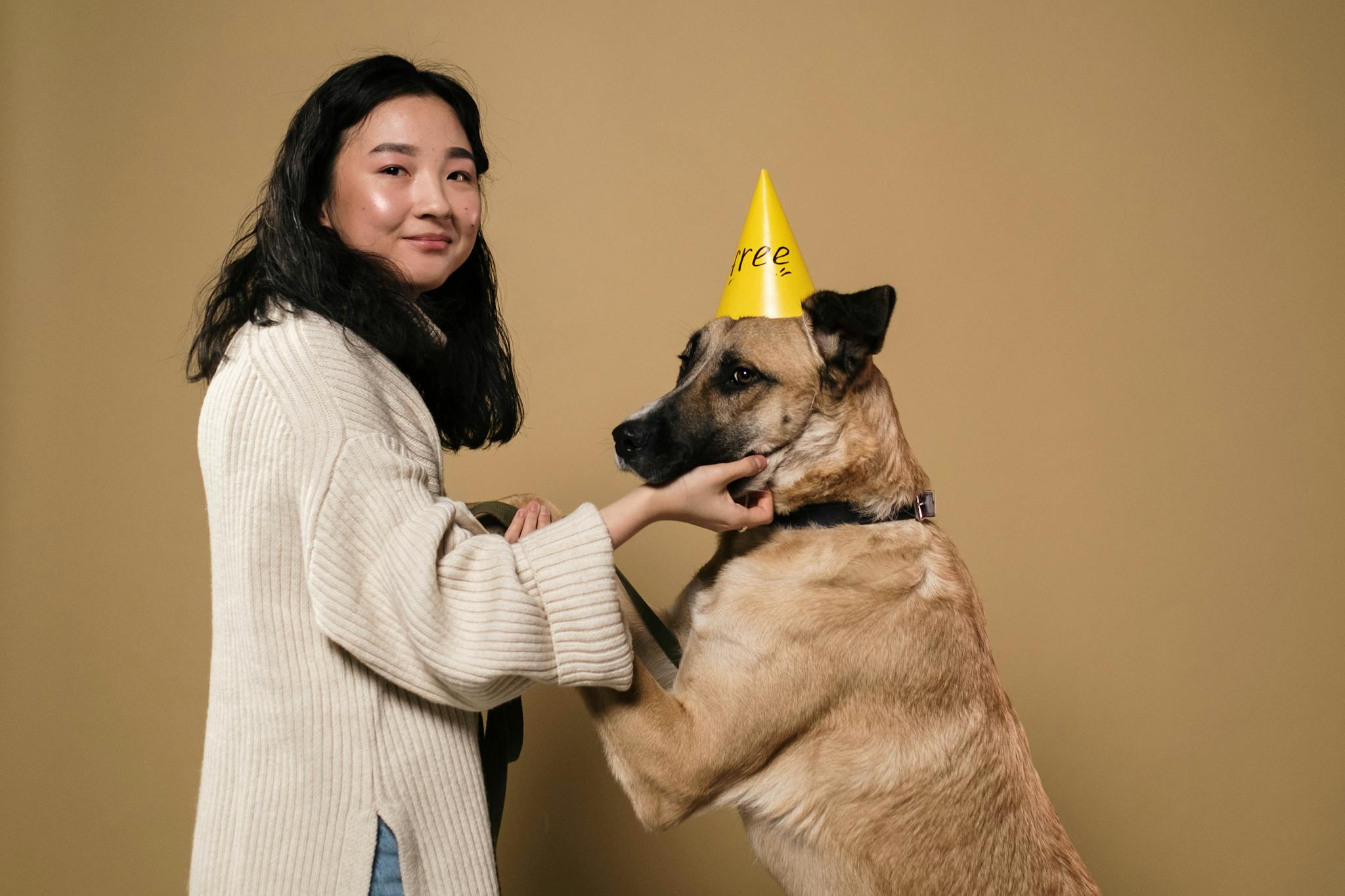 Portrait of woman and dog celebrating with party hat in studio setting.